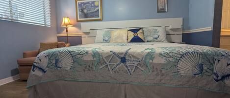 Um quarto com uma cama, mesa de cabeceira, abajur e uma cadeira.