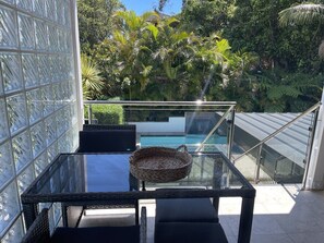 A glass table with wicker chairs and a woven basket, overlooking a pool and lush greenery.