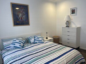 A bedroom with a bed, a nightstand, a dresser, and a painting on the wall.
