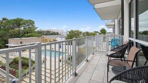 Un balcón con vistas a una piscina, mobiliario exterior y cielo despejado.