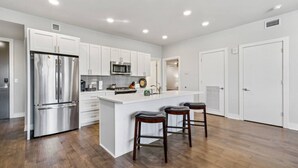 Una cocina moderna con armarios blancos, electrodomésticos de acero inoxidable y una isla central con taburetes de bar.