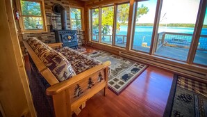 A cozy cabin interior with a stone fireplace, wooden furniture, and large windows overlooking a lake.