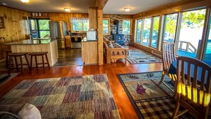 A cozy cabin interior with a kitchen, dining area, and large windows offering views of the outdoors.