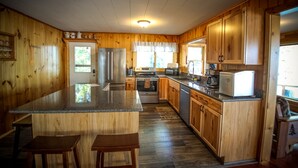 A kitchen with wooden cabinets, a granite countertop, stainless steel appliances, and a window with a view of greenery.