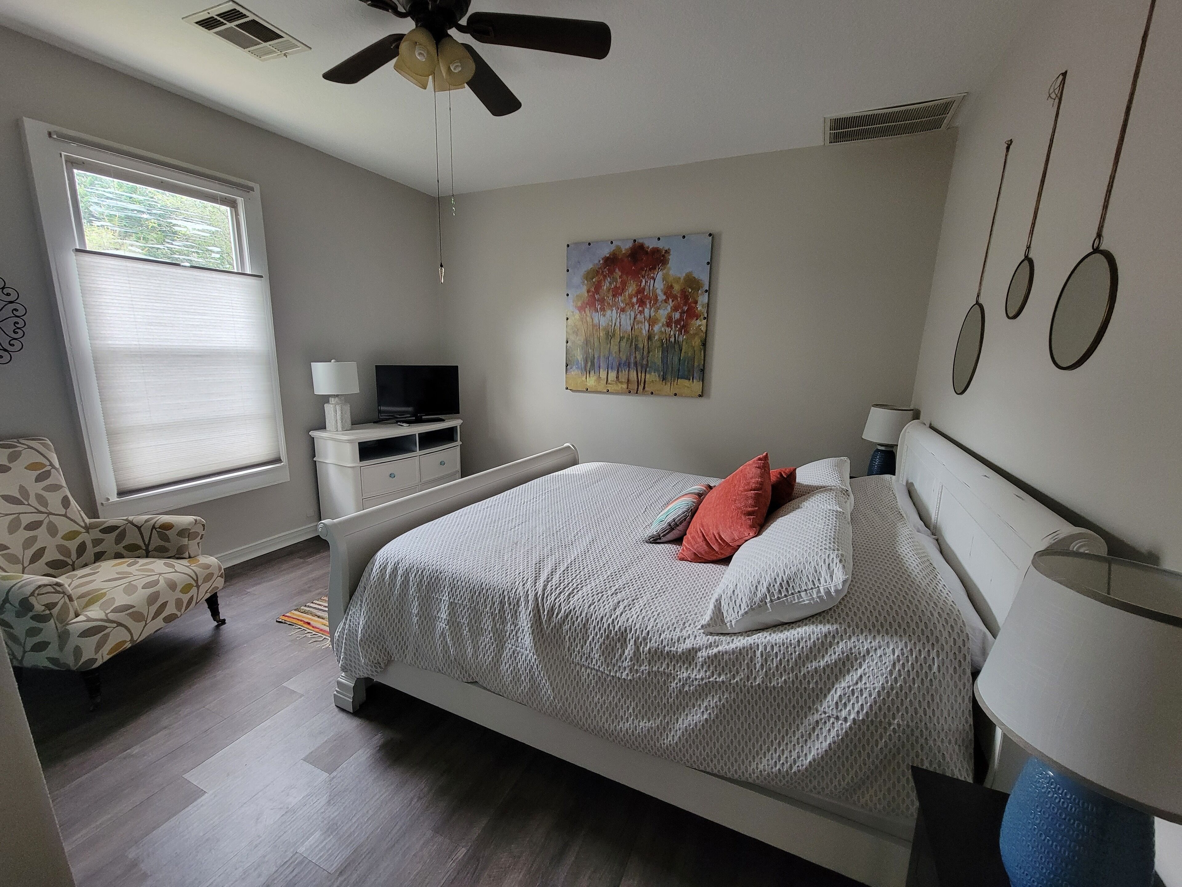 A bedroom with a bed, a chair, a TV, and a painting on the wall.