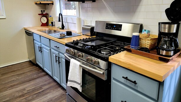 A modern kitchen with a stainless steel stove, a coffee maker, and wooden countertops. - Historic 3 bed, 2bath Bungalow Minutes from IAH with Backyard Putting Green! (Humble)