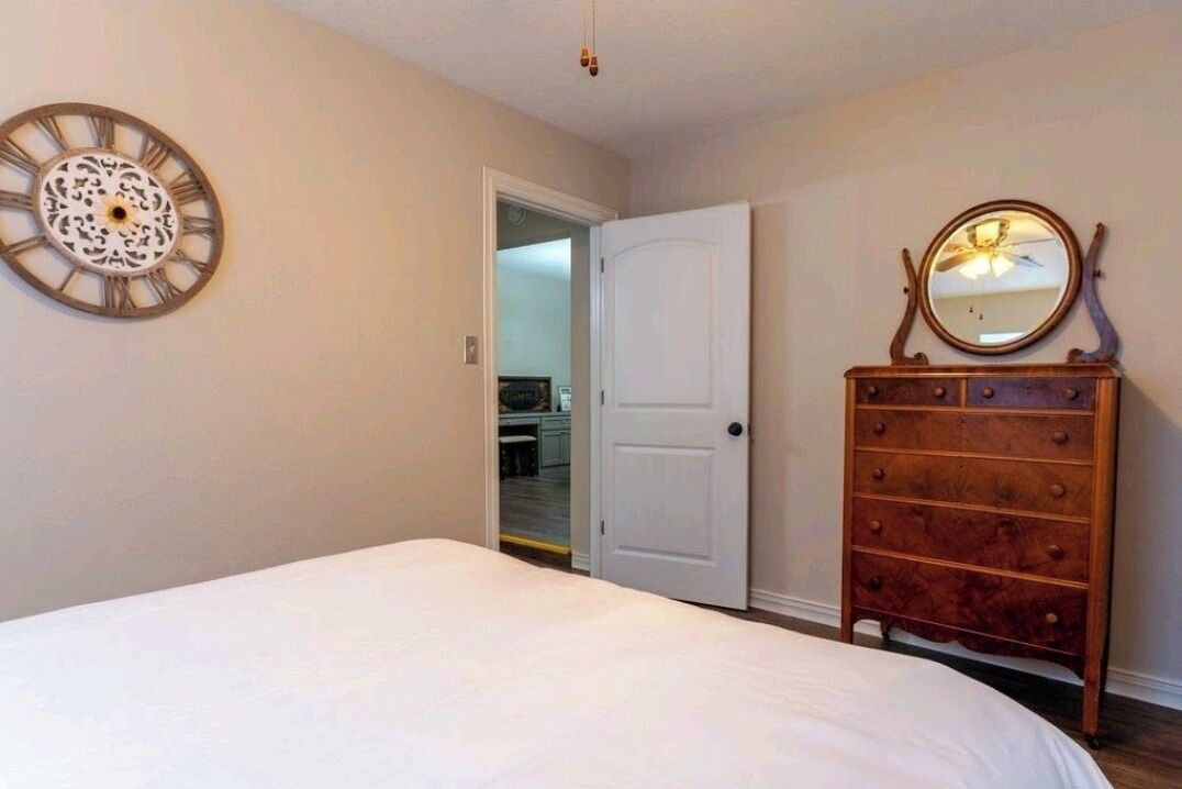 A bedroom with a bed, a dresser, a door, and a wall clock.