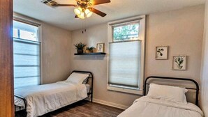 A bedroom with two single beds, a ceiling fan, and a window with blinds. - Historic 3 bed, 2bath Bungalow Minutes from IAH with Backyard Putting Green! (Humble)