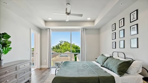 Ein Schlafzimmer mit einem Bett, einem Schminktisch, einem Deckenventilator und einem Balkon mit Blick auf Häuser.