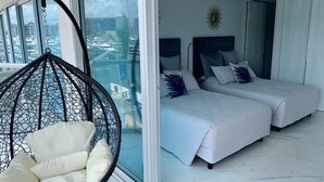 A modern hotel room with a large balcony, two beds with white bedding, a hanging chair with cushions, and a city view. - Amazing Loft in the Marina (Puerto Vallarta)