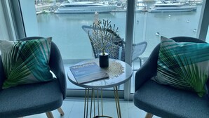 A modern room with a view of a marina, featuring two grey armchairs with patterned cushions, a small round table with a magazine, and a decorative branch. - Amazing Loft in the Marina (Puerto Vallarta)