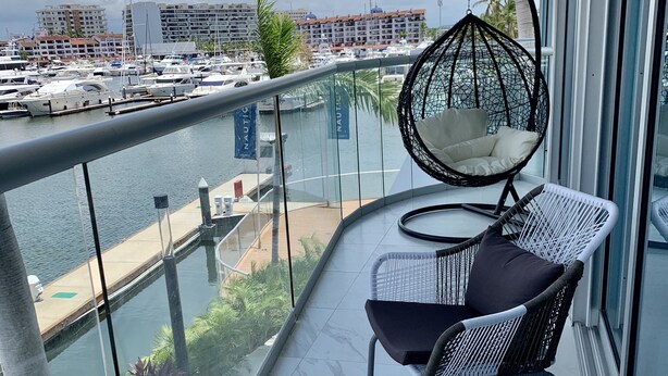 A balcony with wicker chairs and a hanging chair overlooking a marina with boats and buildings. - Amazing Loft in the Marina (Puerto Vallarta)