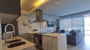 A modern kitchen with a built-in island, stainless steel appliances, and a large window with blinds. - Amazing Loft in the Marina (Puerto Vallarta)