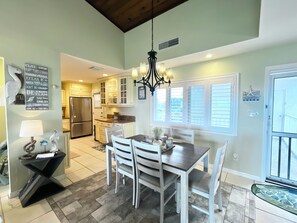 A dining area with a table and chairs, a chandelier, and a kitchen in the background. - CP 334 Ocean View Condo - Vacation Rental in Ocean Village (Fort Pierce)