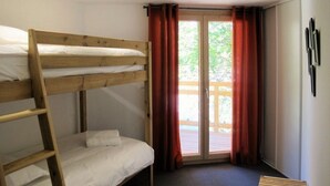 Een slaapkamer met een stapelbed, een houten ladder, een schuifdeur met rode gordijnen en een kleine houten bank.