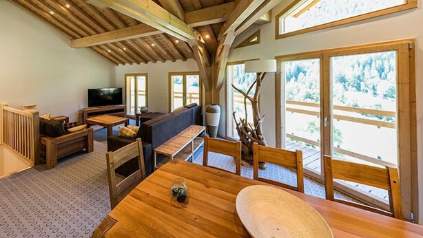Een gezellige woonkamer met houten balken, een bank, een televisie en een eettafel met stoelen.