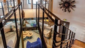 A modern interior with a glass-walled staircase leading to a living area with sofas and a coffee table.