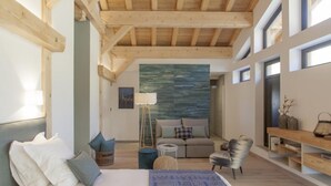 A modern bedroom with a large bed, a sofa, a chair, and a small table. There is a window and a wall with a textured design.