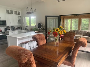 A modern kitchen with white cabinets, a large island, and a dining area with patterned chairs and a wooden table.