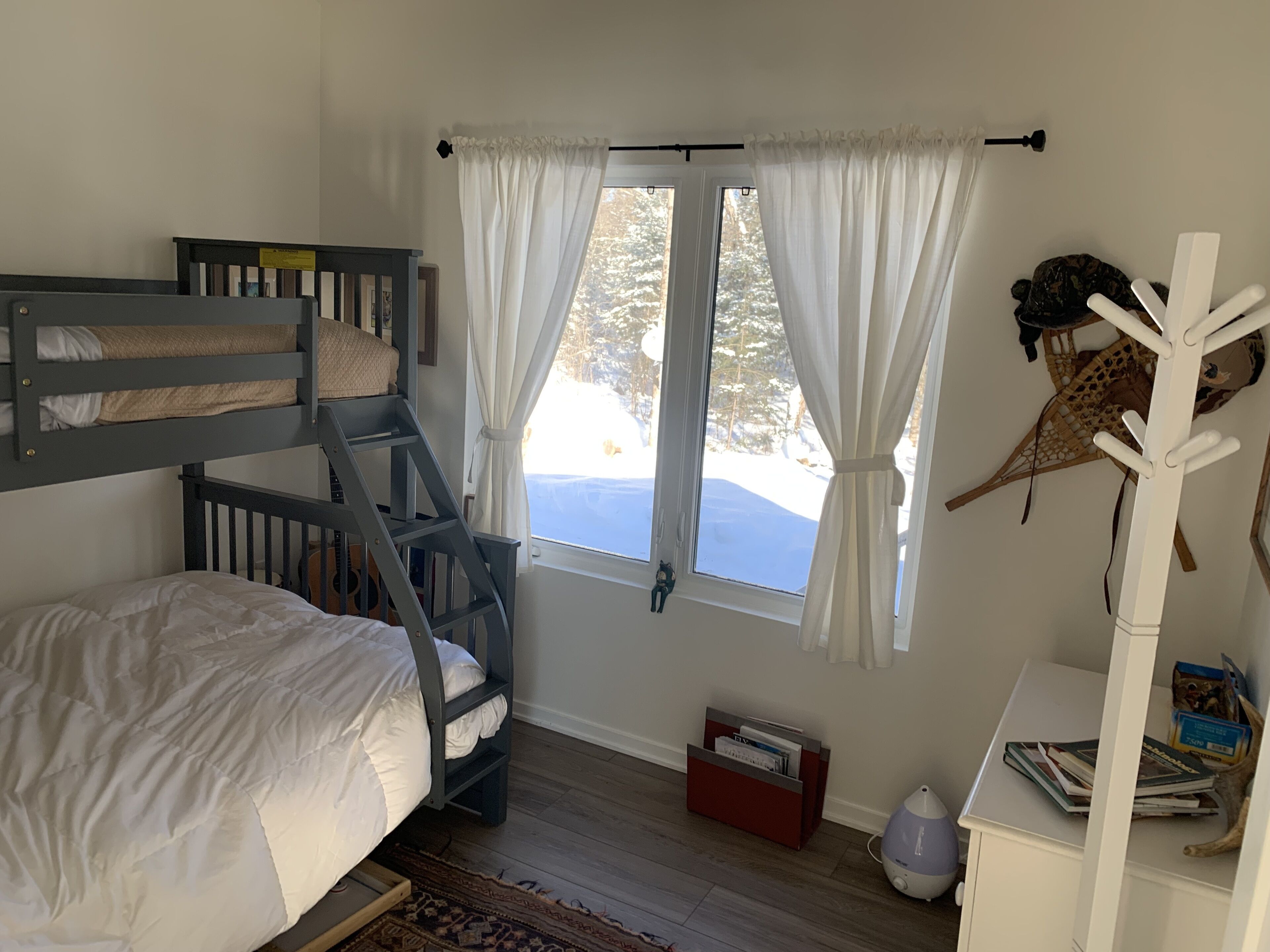 Une chambre avec un lit superposé, un bureau avec une chaise, une fenêtre avec des rideaux et un porte-manteau.