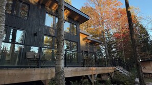 A modern wooden cabin with large windows and a deck. - Muskoka River Retreat – A Year-Round Paradise (Bracebridge)