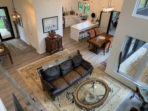 A spacious living area with a leather sofa, a coffee table, and a dining table with chairs. There is a kitchen in the background with white cabinets and a large window.
