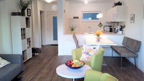 A modern living room with a sofa, a round table with a fruit bowl, and a kitchen area with a dining table and chairs.
