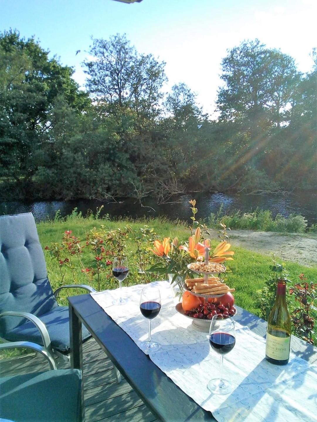 Una mesa para comer al aire libre con una botella de vino, dos copas de vino tinto, un frutero y una silla.