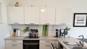 A modern kitchen with white cabinets, a built-in oven, a dishwasher, and a coffee maker.