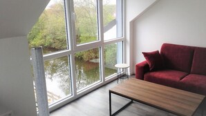 Ein Zimmer mit einem großen Fenster, einem roten Sofa und einem kleinen Tisch.