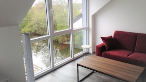 Een kamer met een groot raam, een rode bank en een kleine tafel.