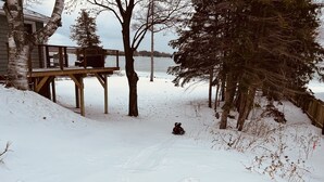 A snowy deck area with a sledding path leading to a body of water. - Private Elk Lake Cottage minutes from Elk Rapids (Kewadin)