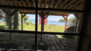 A view through a window with a wooden structure and a grassy area in front of a body of water. - Private Elk Lake Cottage minutes from Elk Rapids (Kewadin)