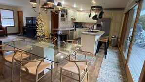 A modern kitchen with a central island, pendant lighting, and a dining area with a glass table and chairs. - Private Elk Lake Cottage minutes from Elk Rapids (Kewadin)