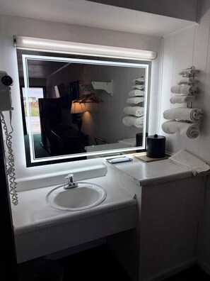 A bathroom with a large mirror, a sink, and a towel rack.