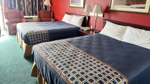 A hotel room with two beds, a desk, a chair, and two paintings on the wall.