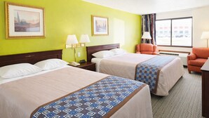 A hotel room with two beds, a chair, a desk, and a window with a view of parked cars.