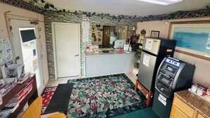 A small, compact room with a kitchenette, a refrigerator, an ATM, and a desk with a computer.