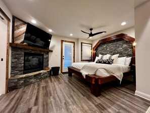 A bedroom with a stone fireplace, a bed with white bedding, and a ceiling fan.