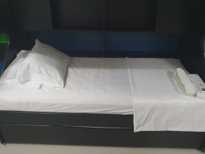 Un lit bien fait, avec des draps blancs, une serviette enroulée et un oreiller.