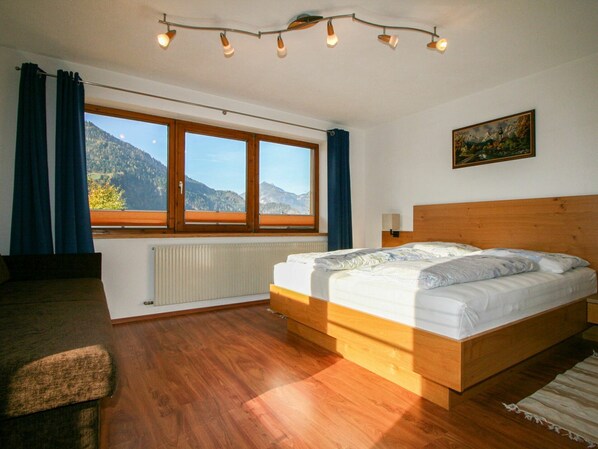 Un dormitorio con cama de madera, vistas a las montañas a través de un ventanal grande y un cuadro en la pared.
