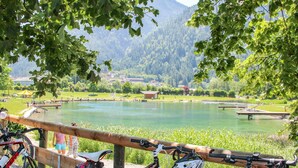 Une vue sur le lac, avec des vélos garés sur une rambarde en bois, donnant sur un lac paisible et une montagne boisée en arrière-plan.