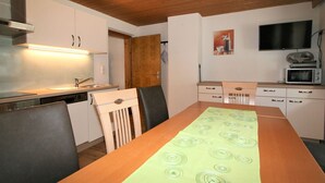 Une cuisine de taille réduite avec des meubles blancs, un plafond en bois et une table à manger recouverte d’une nappe verte.