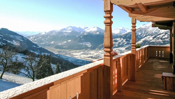 Un balcon en bois offrant une vue sur des montagnes enneigées et une vallée en contrebas.