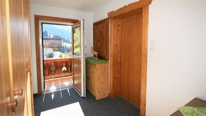 Une pièce en bois avec une porte donnant sur un balcon, une petite table recouverte d’une nappe verte et un luminaire fixé au mur.