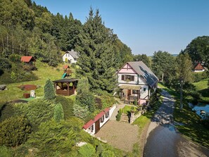 A large two-story house with a sloped roof, surrounded by lush greenery and a small stream. - Lovely apartment in villa for 4 guests with pool, WIFI, TV, patio and pets allowed (Nové Město Nad Metují)