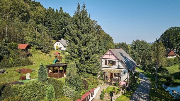 A large two-story house with a sloped roof, surrounded by lush greenery and a small stream. - Nice apartment in villa for 4 people with pool, WIFI, TV, patio and pets allowed (Nové Město Nad Metují)