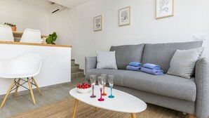 Ein modernes Wohnzimmer mit grauem Sofa, weißem Sessel und einem kleinen weißen Tisch mit bunten Gläsern.