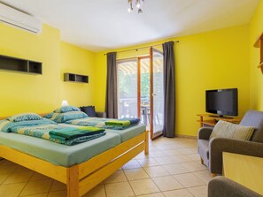 Ein Zimmer mit Bett, Fernseher, Sofa und einem Balkon mit Vorhängen.