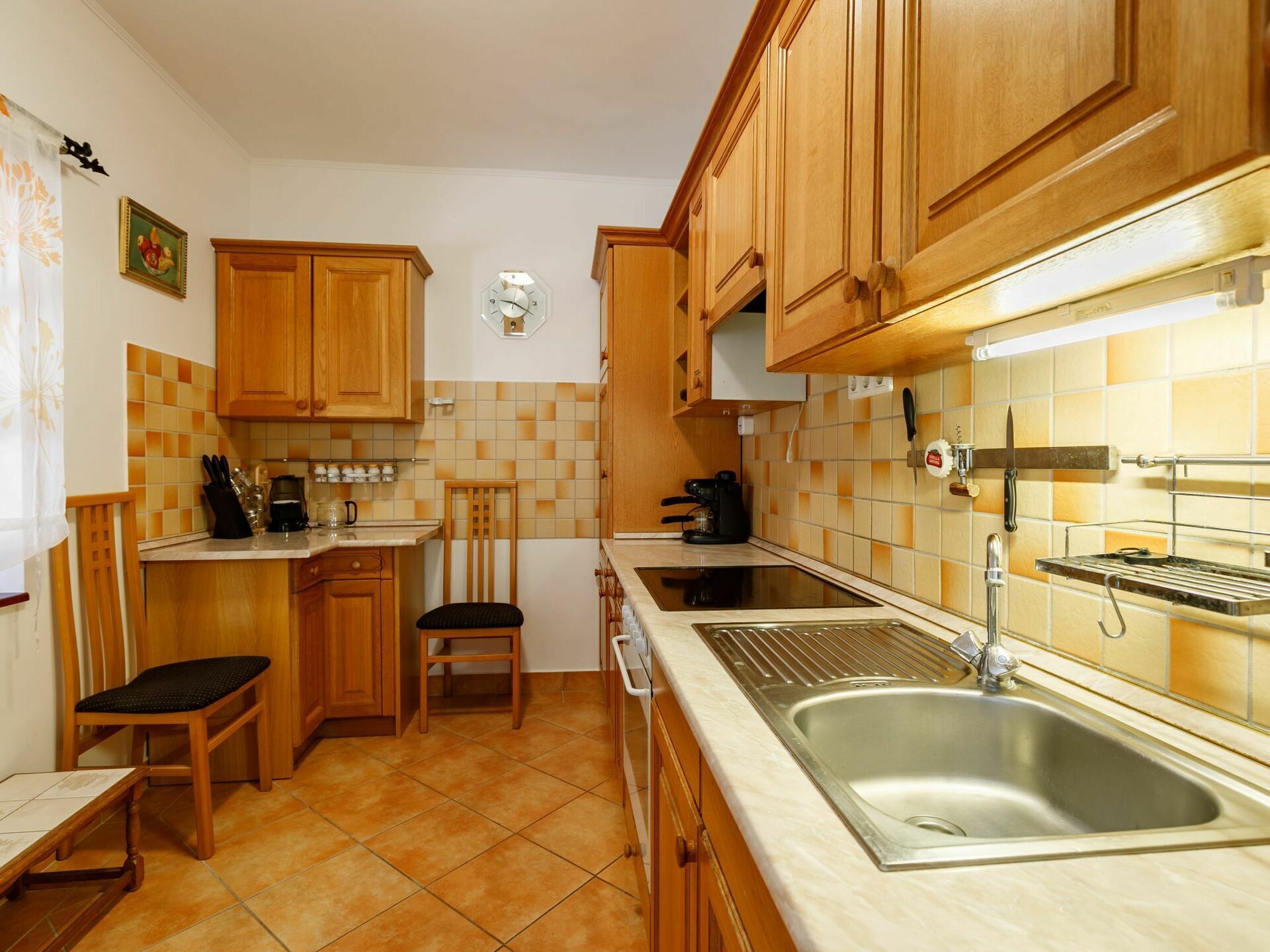 Una cocina con muebles de madera, un lavamanos, una cafetera y una silla.